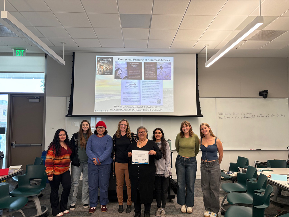 photo of eight people standing in front of a projector screen displaying text about Chumash stories